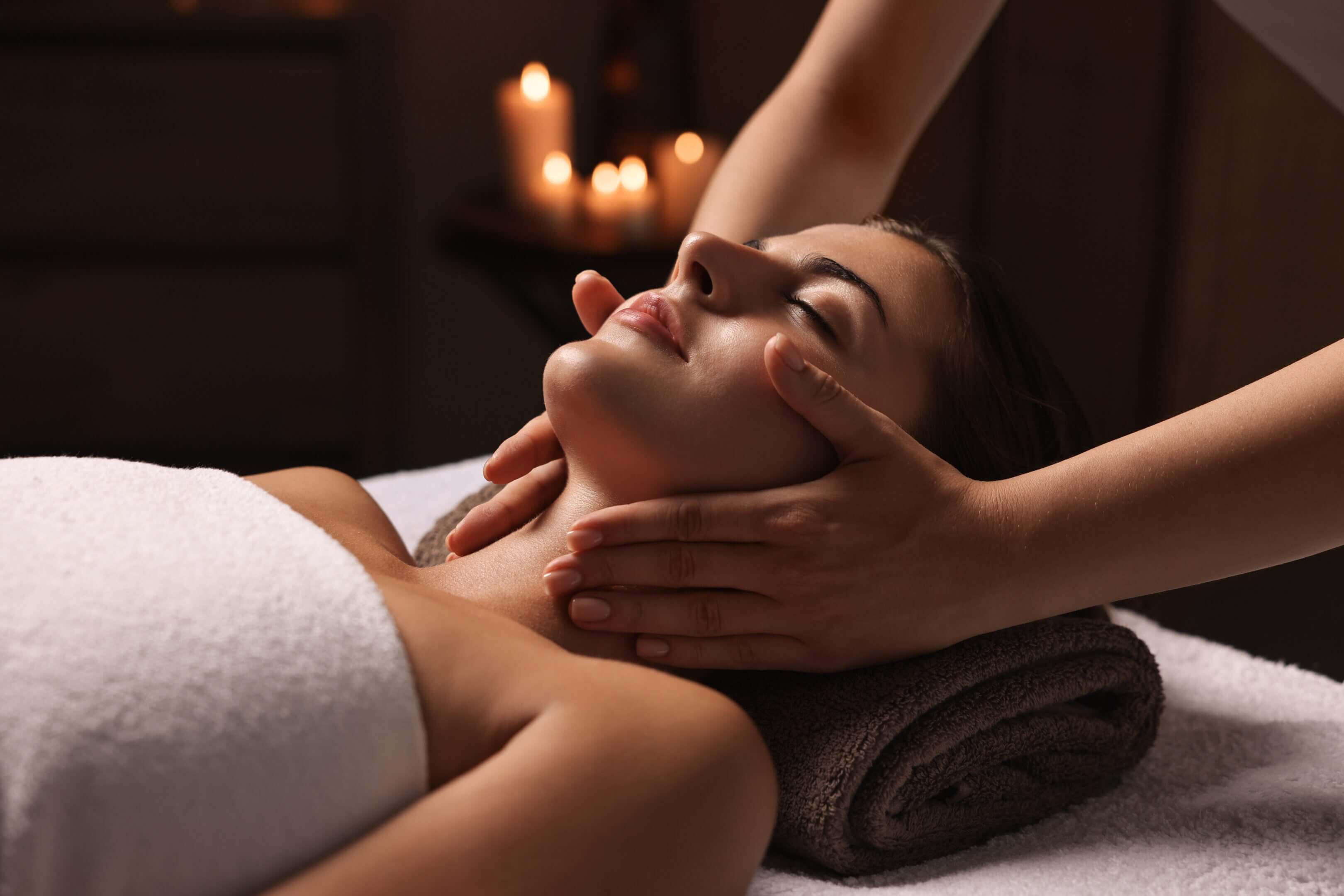 Woman receiving facial massage with candles lit.